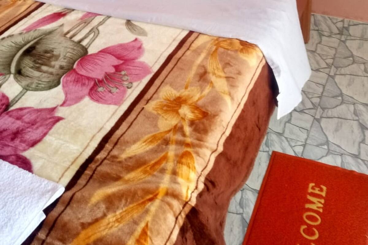 A bed with a floral bedspread, white pillows, and a wooden headboard with heart cutouts. A red welcome mat is visible on the floor.