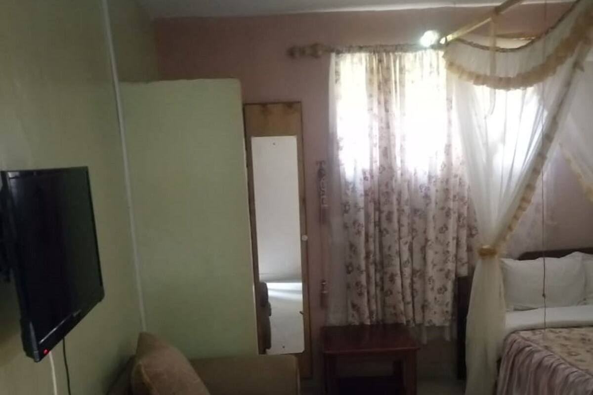 A room with a wooden table, a bed with a canopy, a television mounted on the wall, and a door leading to another room.