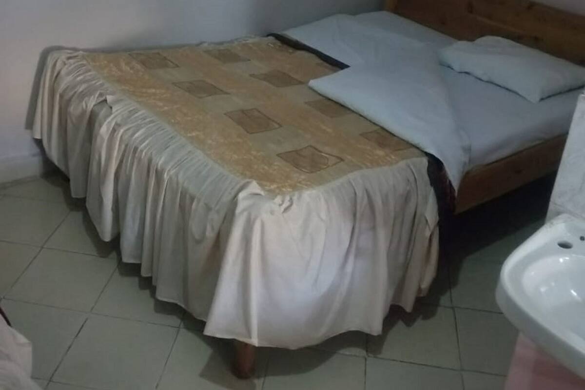A small, single-bed room with a wooden headboard, a patterned bedspread, and a white wall.