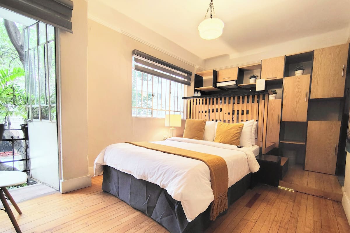 Un dormitorio moderno con una cama grande, suelo de madera, una ventana con persianas y armarios empotrados de madera.