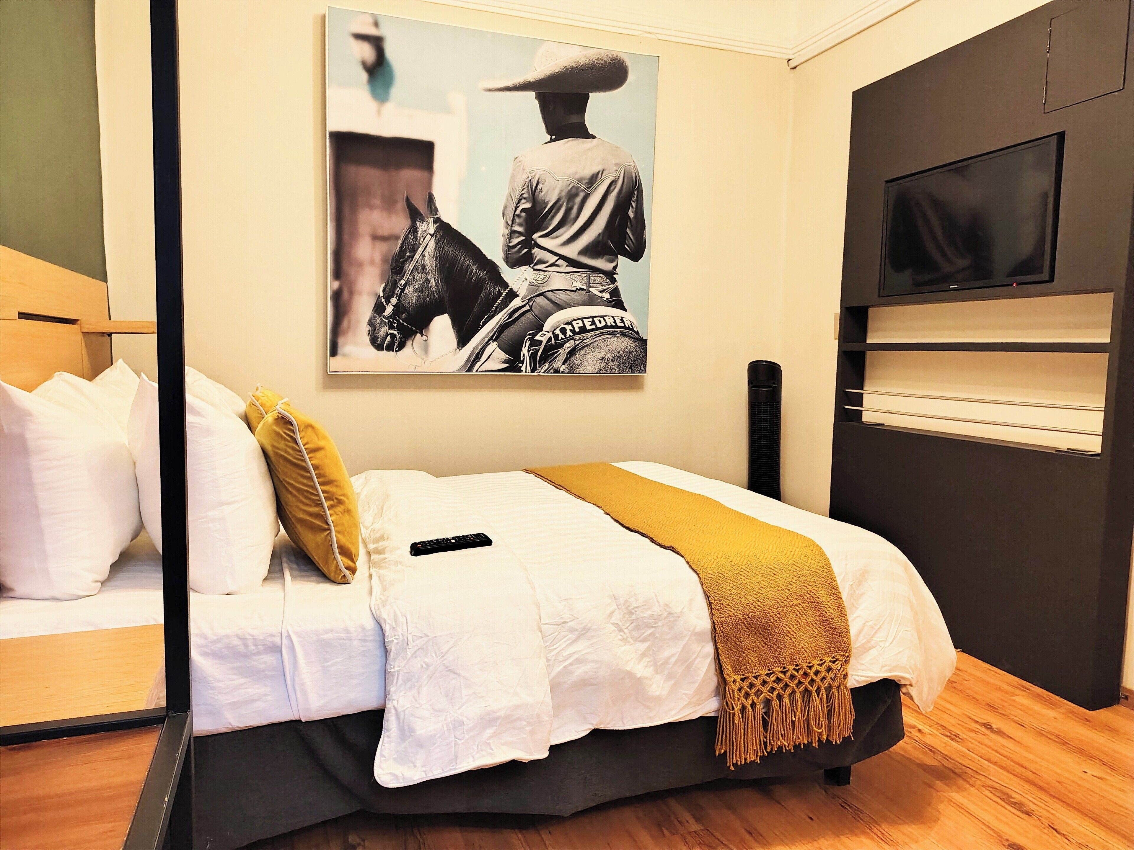A bedroom with a bed, pillows, a blanket, a mounted TV, and a wall-mounted artwork.