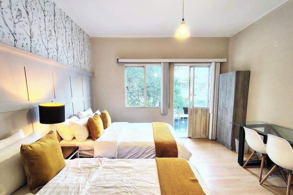 Una habitación de hotel con dos camas, un escritorio, una silla, una lámpara y un ventanal grande.