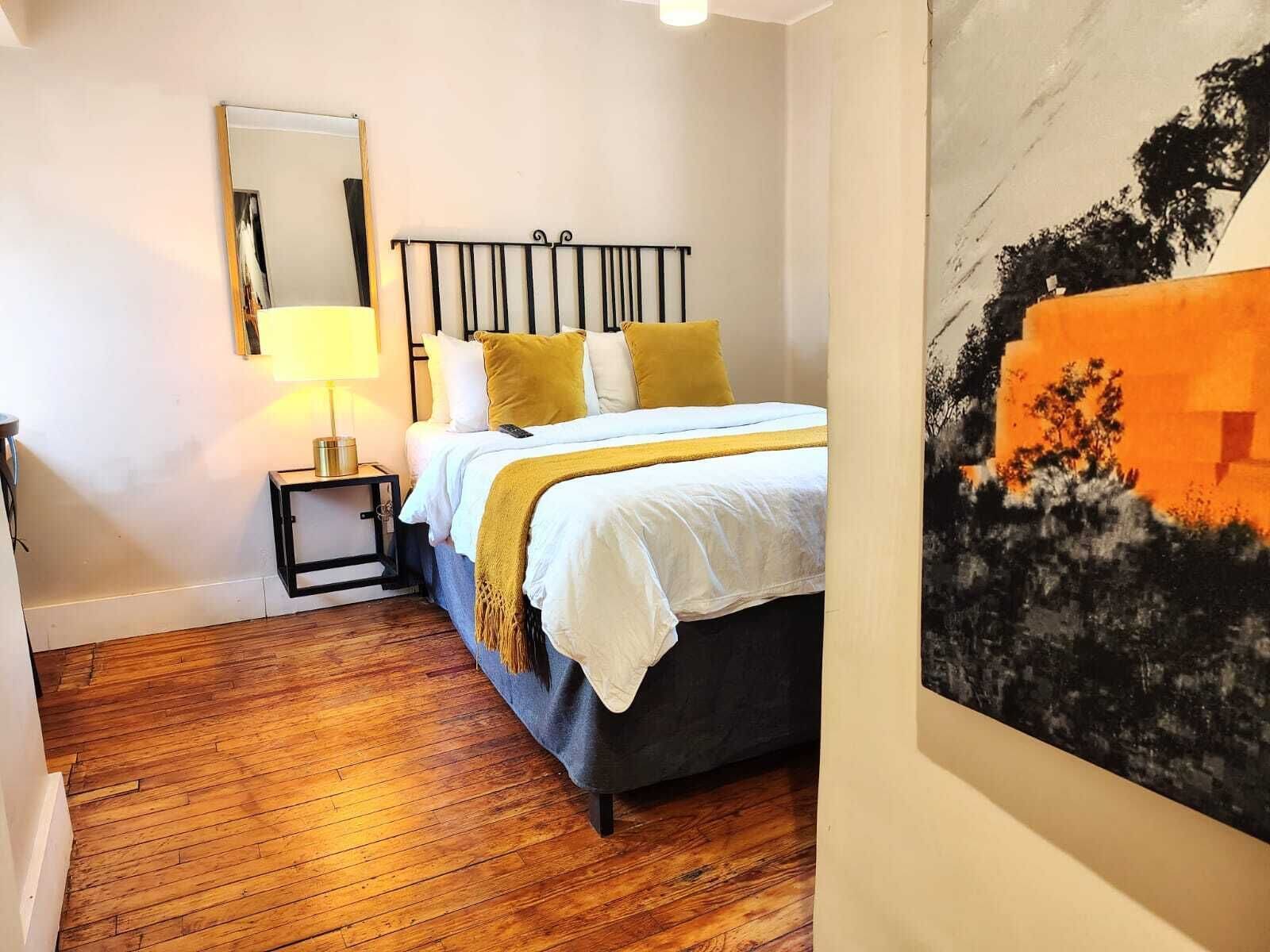 A bedroom with a bed, a nightstand, a lamp, and a painting.