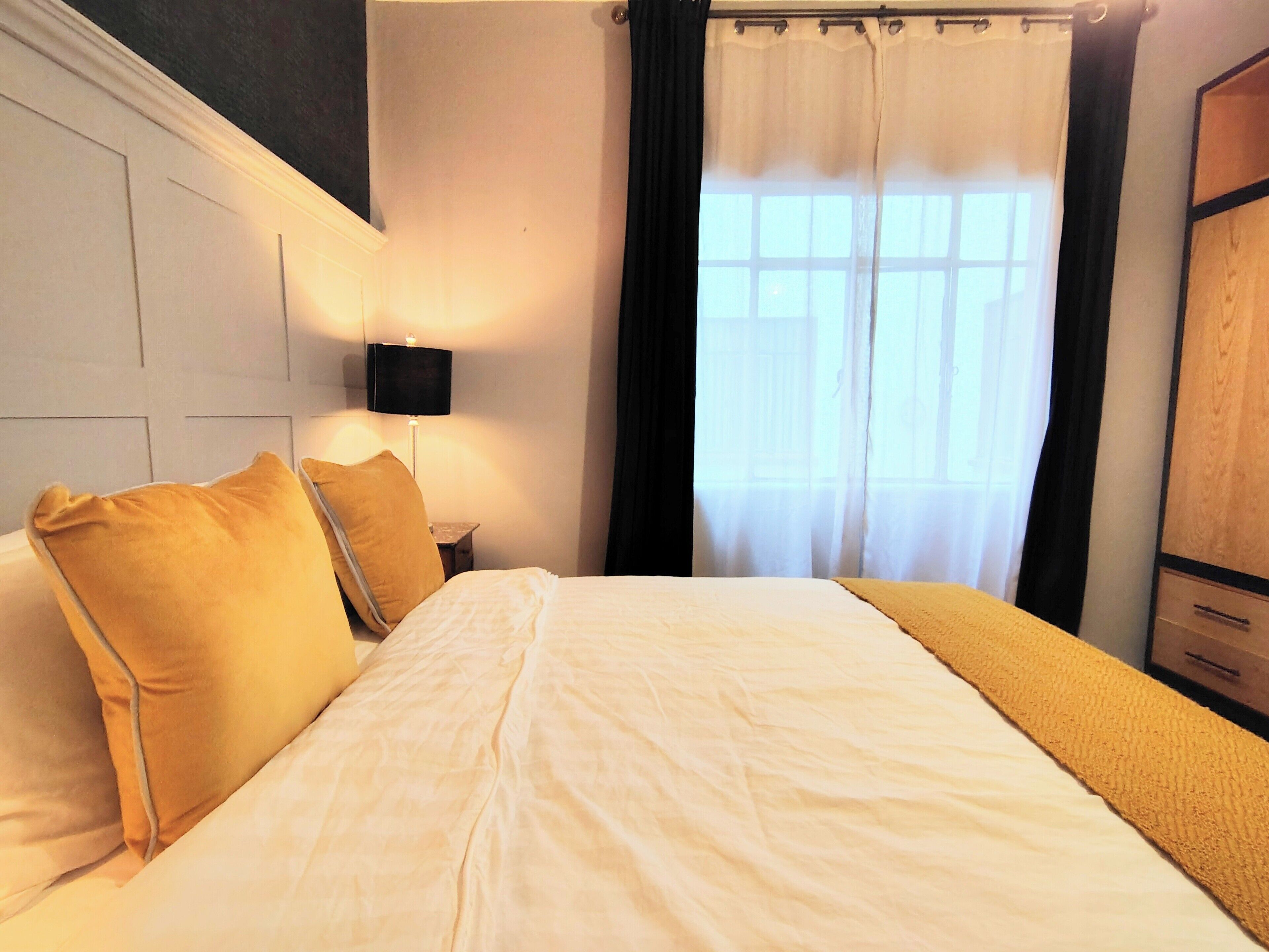 Une chambre d’hôtel avec un grand lit, une table de chevet, une lampe et une fenêtre avec des rideaux.