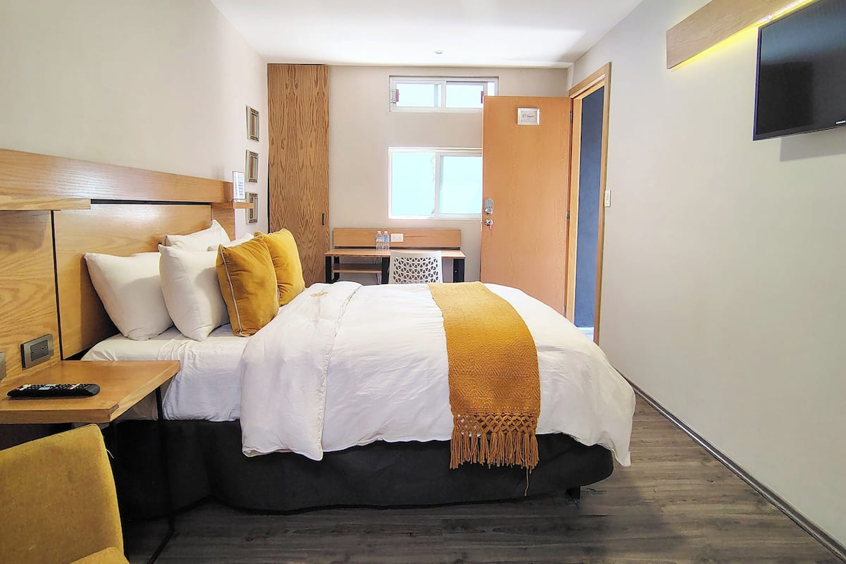 Una habitación de hotel con cama, mesita de noche y televisor montado en la pared.