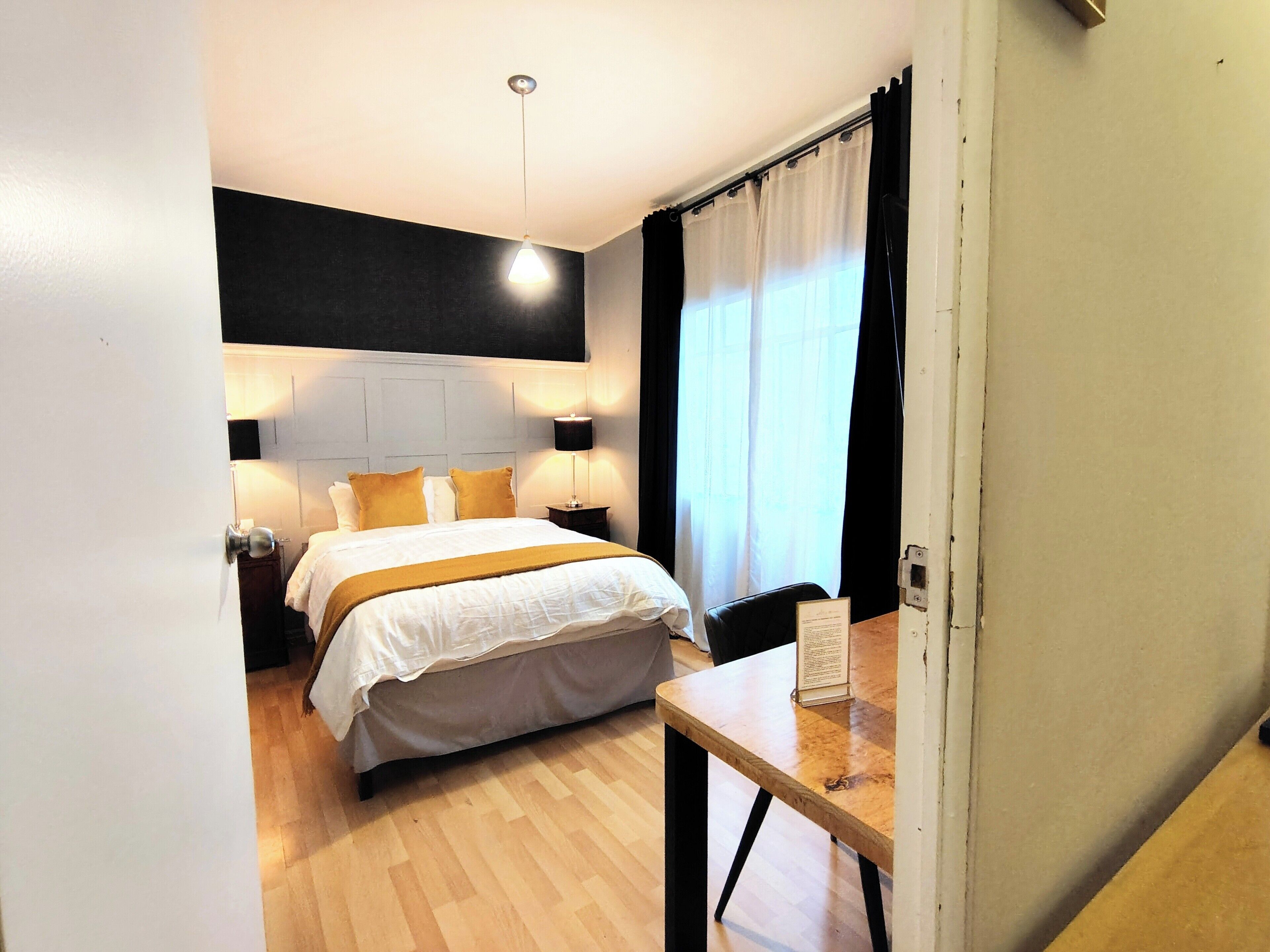 A bedroom with a bed, bedside tables, a desk, and a lamp.