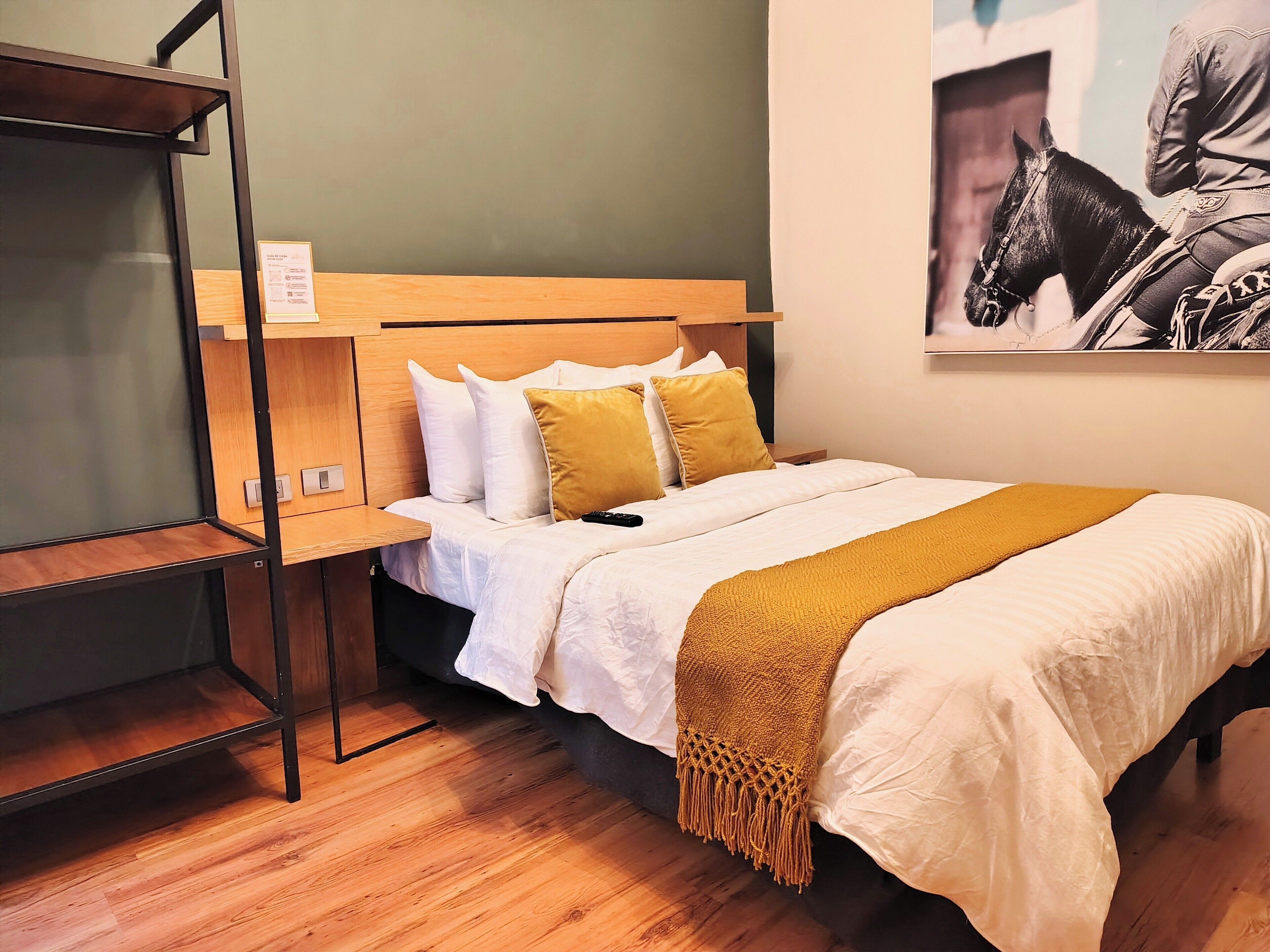 A neatly made bed with a wooden headboard, a bedside table, and a wall-mounted shelf.