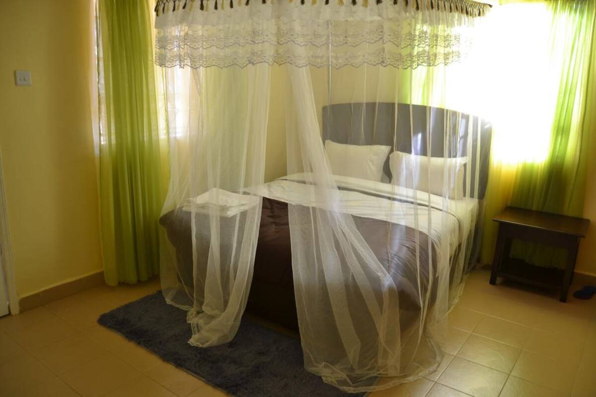 Un dormitorio con cama bajo dosel, mesita de noche y ventana con cortinas.