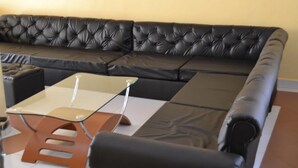 Un salon moderne avec un canapé en cuir noir, une table basse en verre et une table d’appoint en bois.