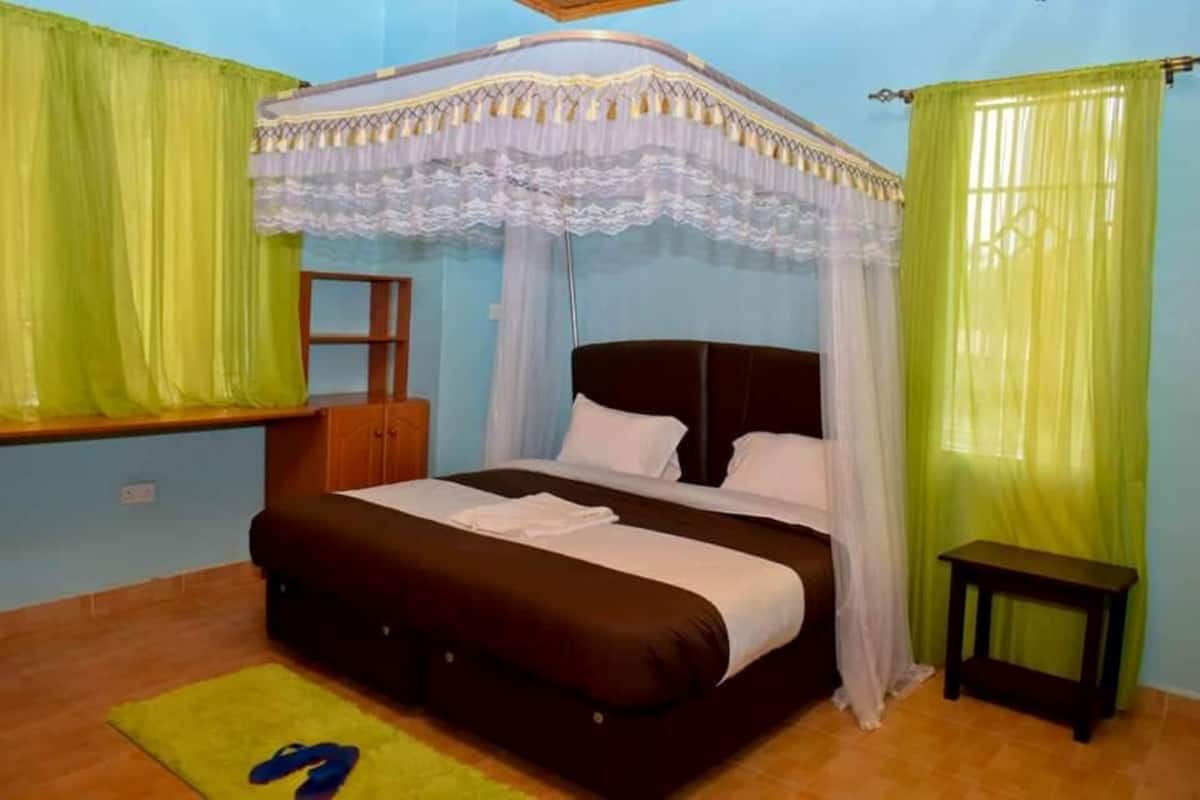 Un dormitorio con una cama, una mesita de noche, una ventana con cortinas y un cabecero de madera.