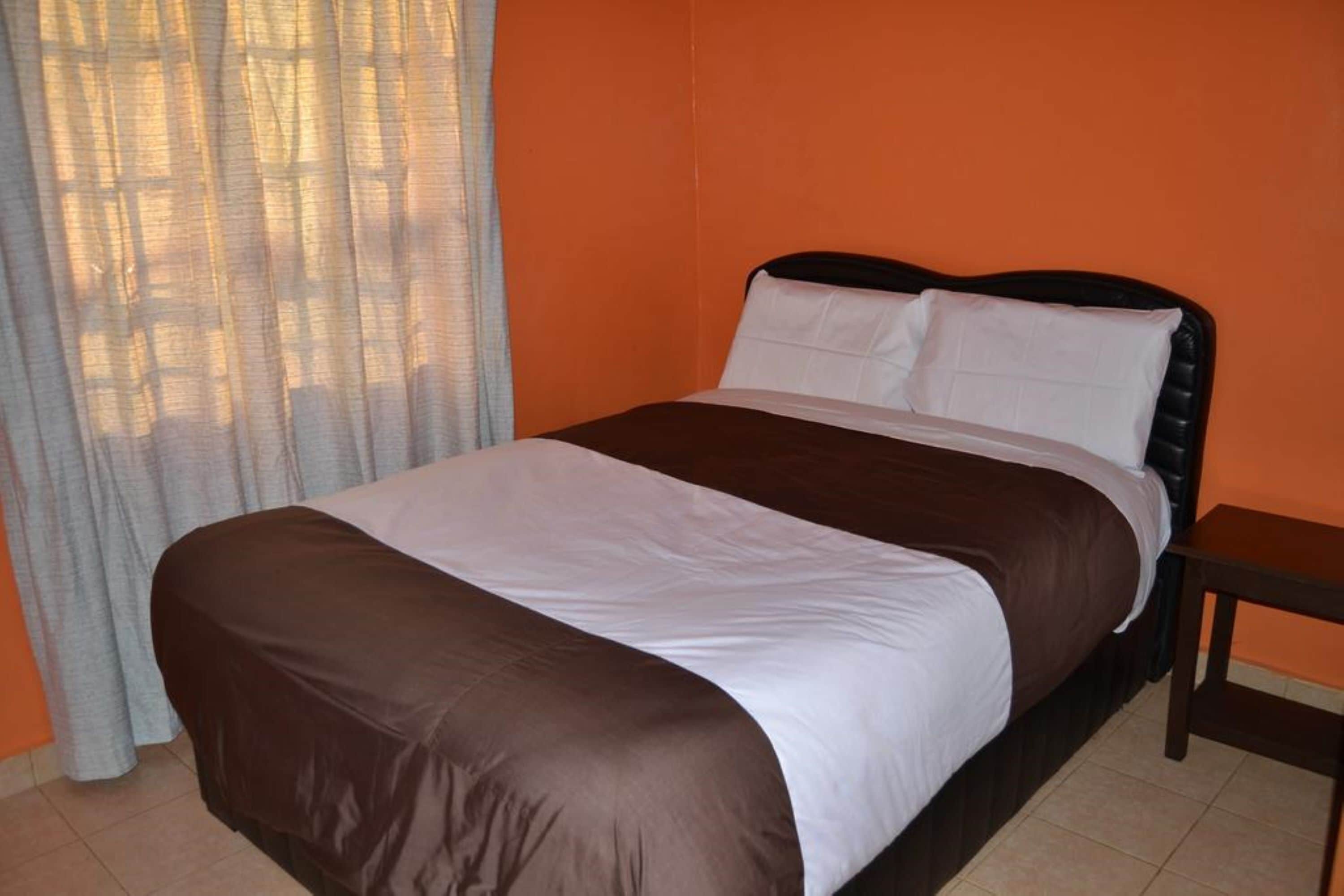 A neatly made bed with a brown and white bedspread, a wooden nightstand, and a window with sheer curtains.