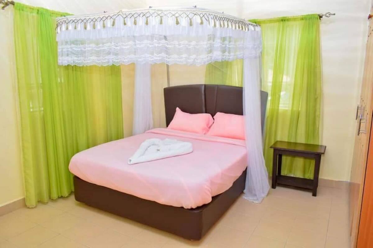 Una cama con dosel, una mesita de noche y cortinas verdes.