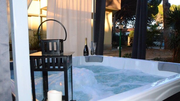A hot tub with a candle and a bottle, surrounded by a wooden deck and greenery. - Bungalow in an artistic villa (Mondello, Pa, Italy) beachfront, sea and city (Palermo)