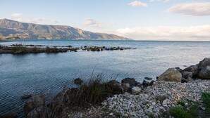A coastal landscape with a rocky shoreline, calm water, and distant mountains under a clear sky. - Blue House - Recently renovated (corfu)