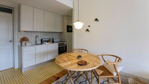 Una cocina compacta con armarios blancos, una mesa redonda de madera y una lámpara colgante.