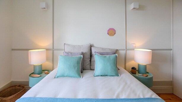 Un dormitorio ordenado con cama, dos lámparas de noche y una lámpara de pared.