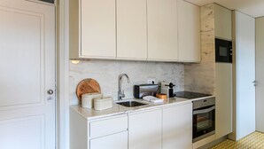 Una cocina compacta con armarios blancos, un protector contra salpicaduras de mármol, horno empotrado y una pequeña encimera con un tostador y un lavabo.