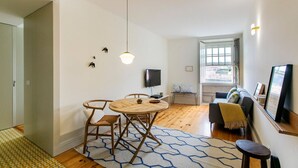 Una sala moderna con una mesa redonda de madera, un sofá y un televisor montado en la pared.