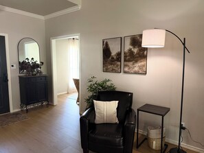A living room with a black leather chair, a floor lamp, and a small table. There is a mirror on the wall and a door leading to another room. - The Willow Oak Large 2400 sf home 3 bed 2 bath (Paris)