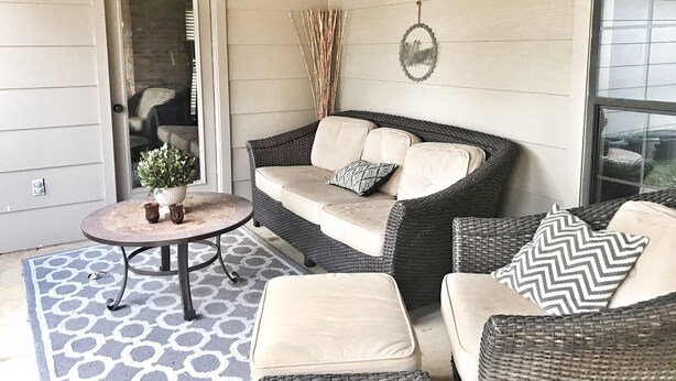 Een gezellig buitenverblijf met een rieten bank, twee comfortabele fauteuils, een klein rond tafeltje en een plant in pot.
