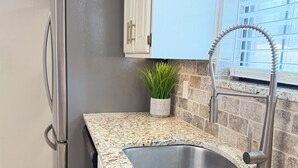 Een keuken met een roestvrijstalen spoelbak, een granieten aanrechtblad en een raam met uitzicht op gebouwen.