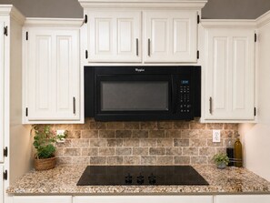 A kitchen with white cabinetry, a black microwave, a granite countertop, and a backsplash.