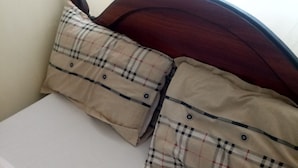 Uma cama com cabeceira de madeira, duas almofadas xadrez e lençol branco liso.