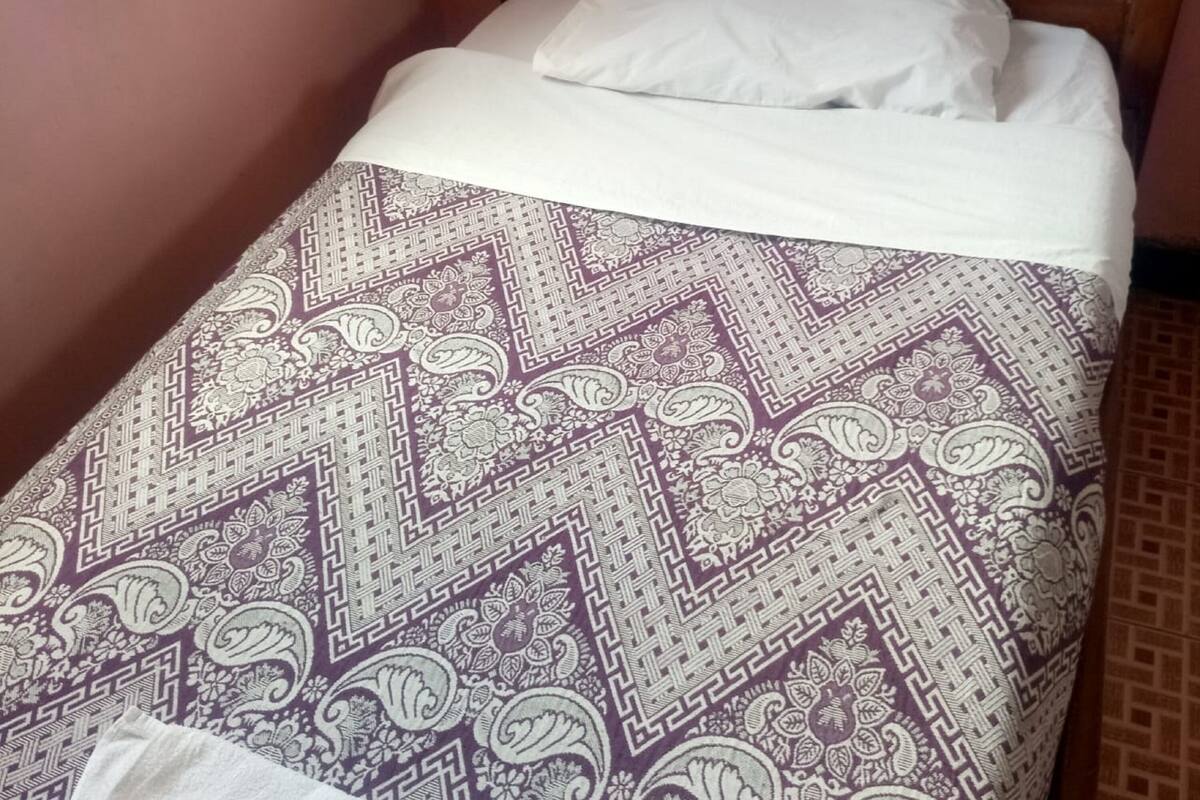 Uma cama de solteiro com colcha estampada e almofadas brancas em um quarto com cabeceira de madeira e paredes cor-de-rosa.