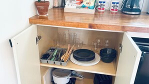 A compact kitchen with a wooden countertop, a potted plant, a coffee maker, and a cabinet containing kitchen utensils and dishes. - Vintage Studio in Artsy, Modern Walkable Montrose Area! (Houston)