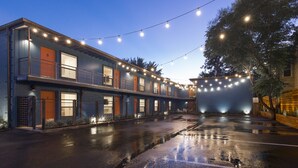 A two-story building with a blue facade, orange doors, and a wet ground, likely after rain. - Vintage Studio in Artsy, Modern Walkable Montrose Area! (Houston)
