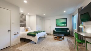 A modern bedroom with a bed, a desk, a green chair, a TV, and a patterned wall. - Vintage Studio in Artsy, Modern Walkable Montrose Area! (Houston)