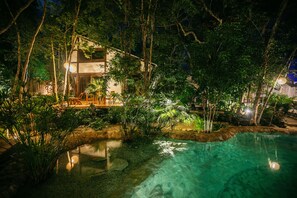 A nighttime view of a house surrounded by lush greenery and a clear pool. - Nahouse Jungle Lodges (Tulum)