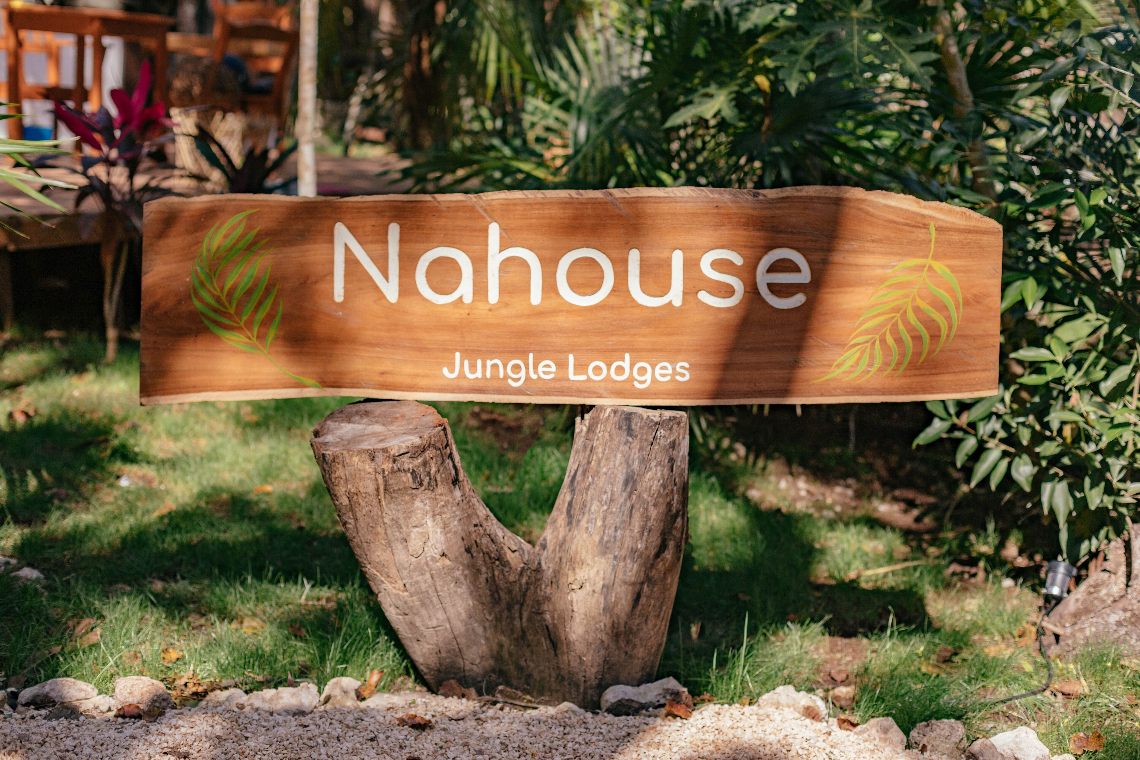 A wooden sign with the text "Nahouse Jungle Lodges" mounted on a tree stump.