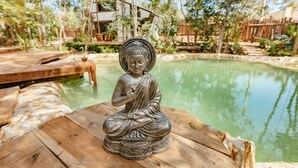 A Buddha statue on a wooden platform by a pond with a wooden deck and trees in the background. - Nahouse Jungle Lodges (Tulum)