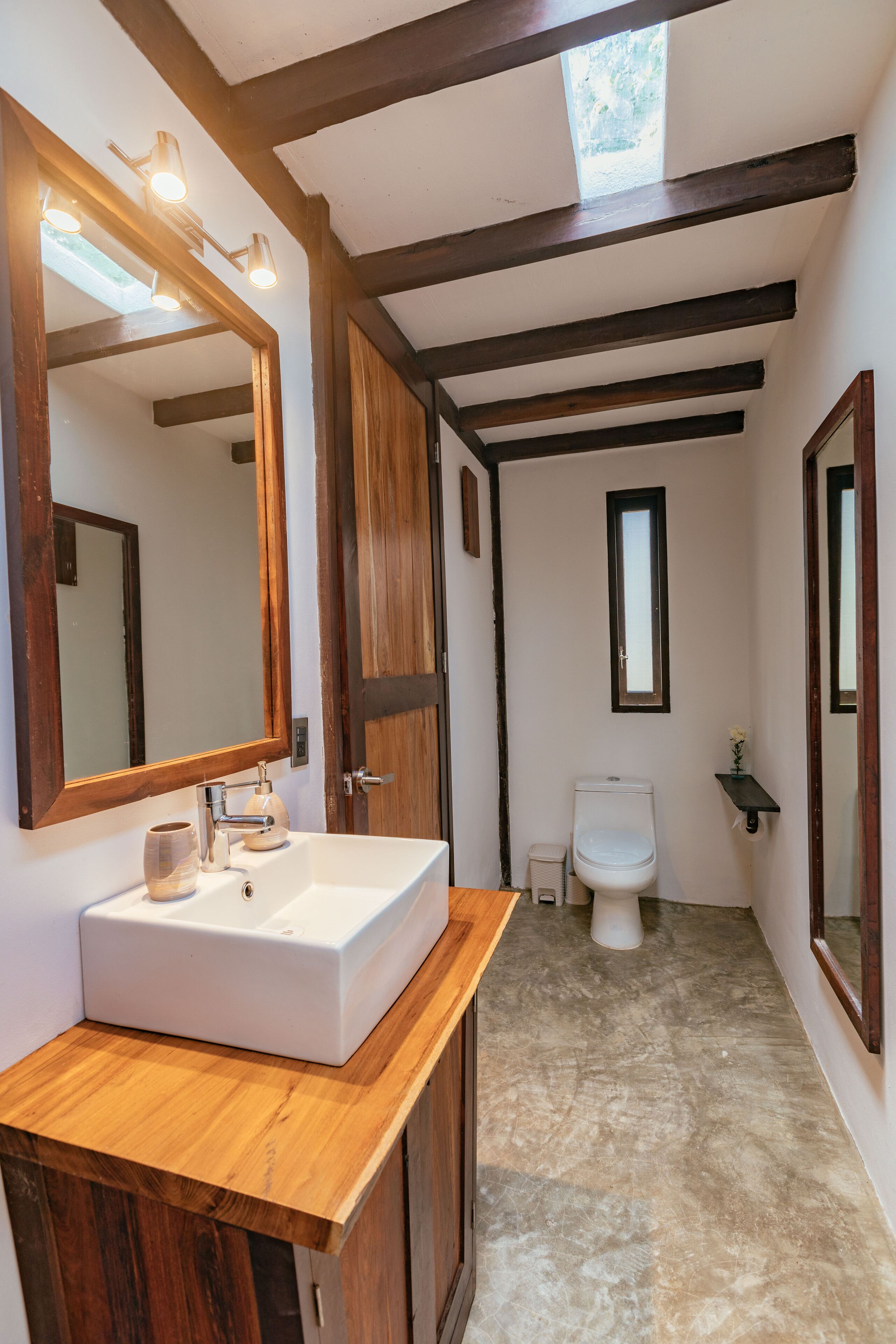 A narrow bathroom with a wooden vanity, a large mirror, a white sink, and a toilet.