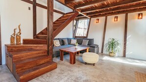 A spacious living area with a wooden staircase, a sofa set, a coffee table, and a potted plant. - Nahouse Jungle Lodges (Tulum)