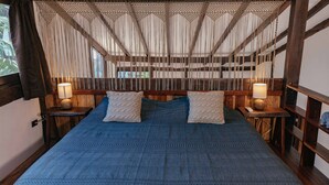 A bed with a blue blanket, two pillows, and a wooden headboard with a woven canopy. There are two bedside tables with lamps. - Nahouse Jungle Lodges (Tulum)