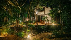 A two-story wooden house surrounded by dense tropical vegetation, with a deck and outdoor seating area. - Nahouse Jungle Lodges (Tulum)