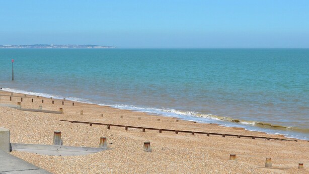 A beach with a pebble shore, wooden barriers, and a clear view of the sea.
