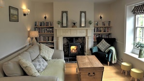 A cozy living room with a fireplace, bookshelves, a sofa, and a window with curtains.