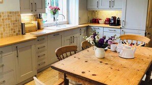 A kitchen with light grey cabinets, a wooden table, and a window with flowers.