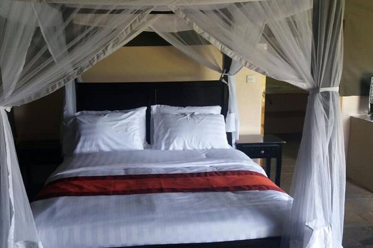 A bed with white linens and a red blanket, a black headboard, and a canopy with sheer curtains.