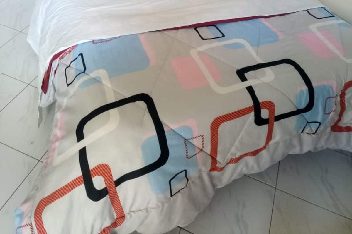 A neatly made bed with a patterned bedspread, a wooden headboard, and white pillows.