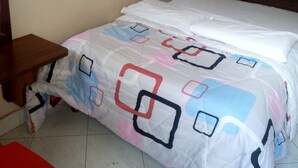 A bedroom with a bed, a wooden nightstand, a red chair, and a white curtain. - Paramount Guest House (Gilgil)