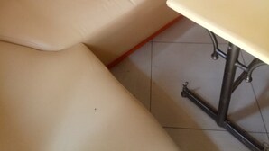 A beige upholstered bench with a tufted backrest, a small table with a metal frame, and a tiled floor. - Paramount Guest House (Gilgil)
