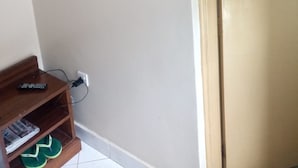 A room with a mounted television on the wall, a wooden shelf with a remote control and magazines, and a door with a light switch. - Paramount Guest House (Gilgil)