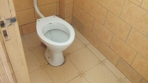 A small bathroom with a toilet, a white tank, and tiled walls. - Paramount Guest House (Gilgil)
