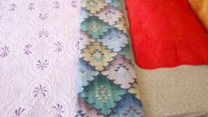 A bed with a patterned bedspread, a red blanket, and a wooden headboard. - Rainbow Guest House (Gilgil)