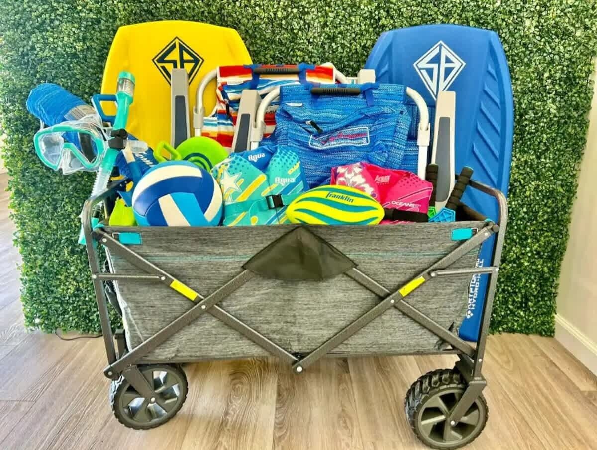 Un carrito de equipaje de viaje lleno de objetos varios, incluyendo un snorkel, una pelota azul y amarilla, y una bolsa azul y blanca.