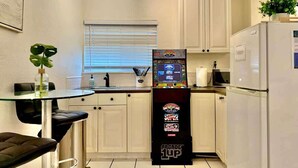 A compact kitchen with white cabinets, a refrigerator, a microwave, and a small dining area with a glass table and two chairs. - MB Studio with Parking Sleeps 4 Steps to Sand (San Diego)